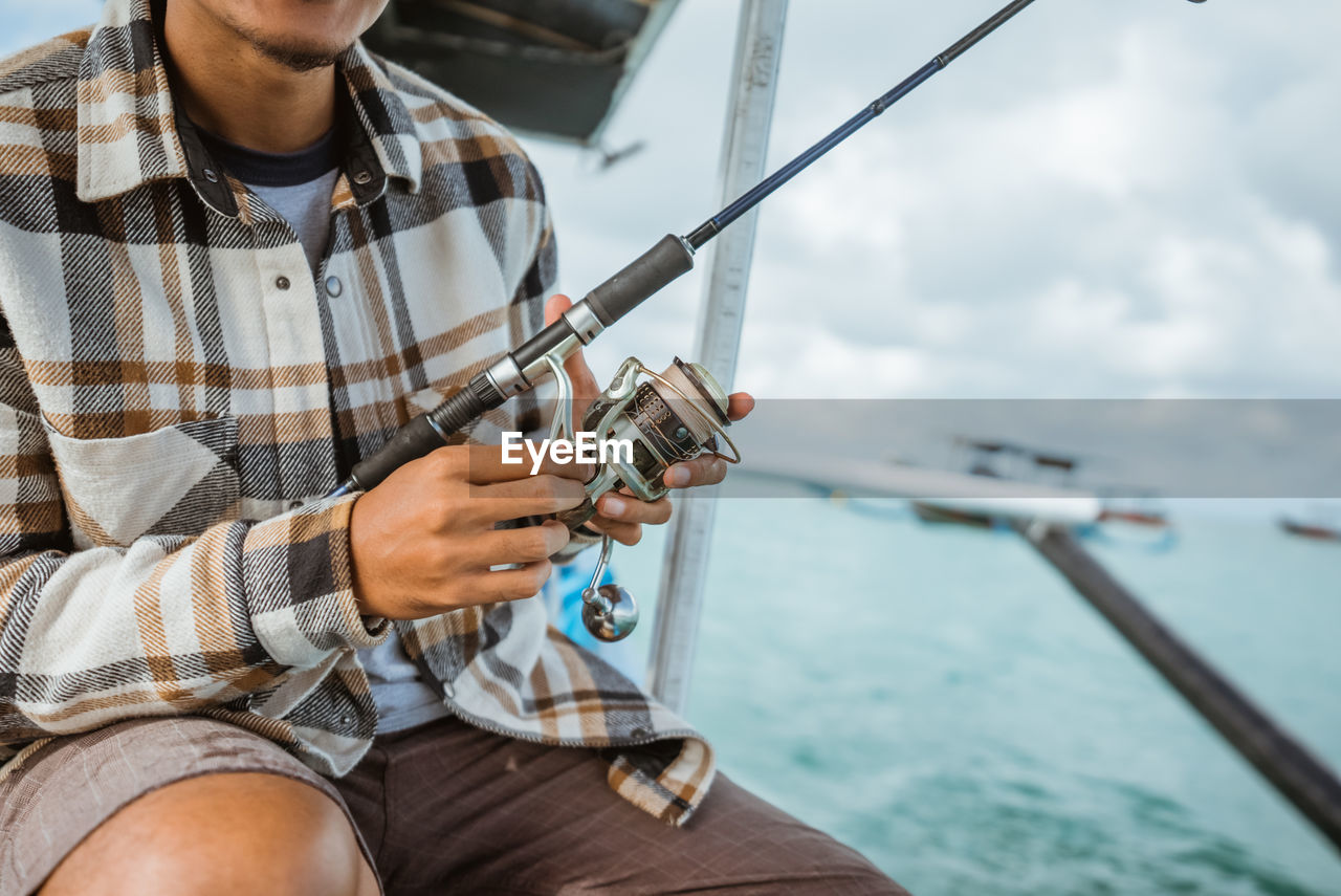 midsection of man using mobile phone while sitting on boat