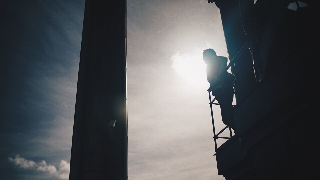 LOW ANGLE VIEW OF SILHOUETTE MAN AGAINST SKY SEEN THROUGH BUILDING