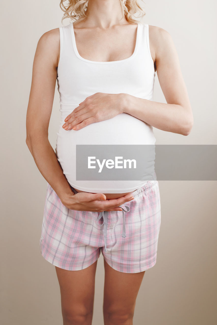 Midsection of pregnant woman touching abdomen against white background