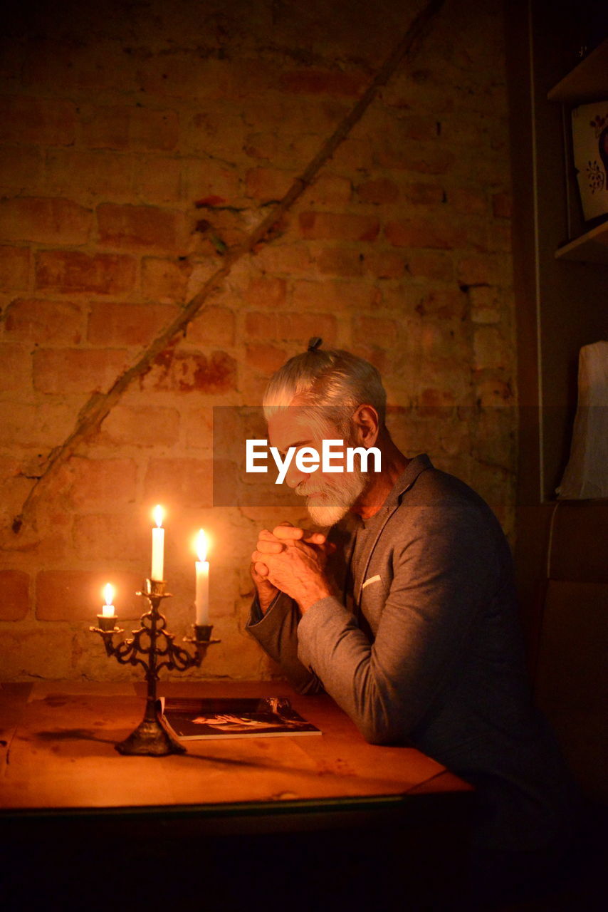 White haired bearded man meditating by candlelight at night