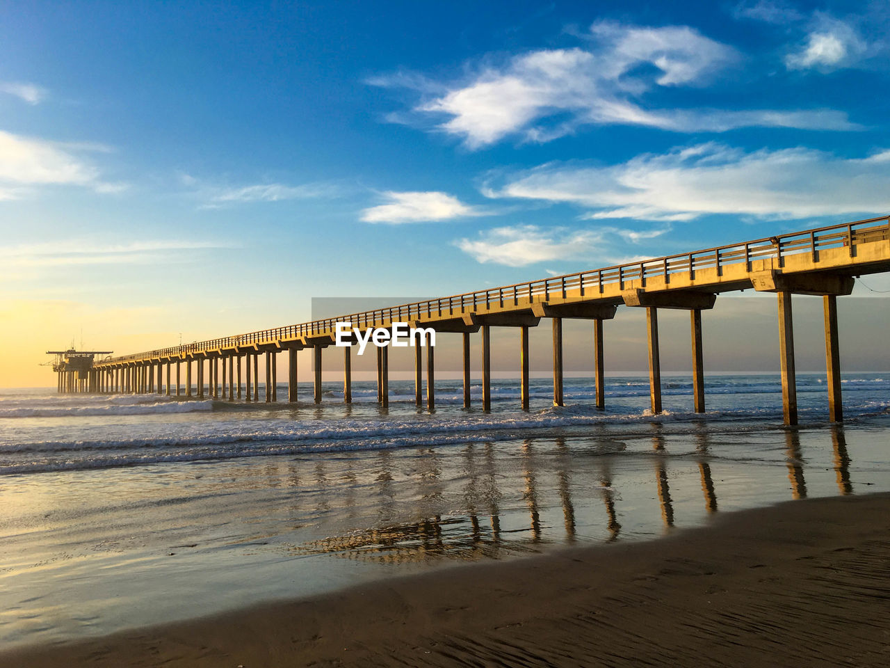 Low angle view of pier at beach against blue sky during sunset