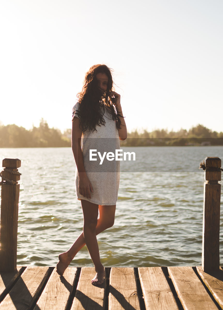 Young woman standing on pier over lake against sky