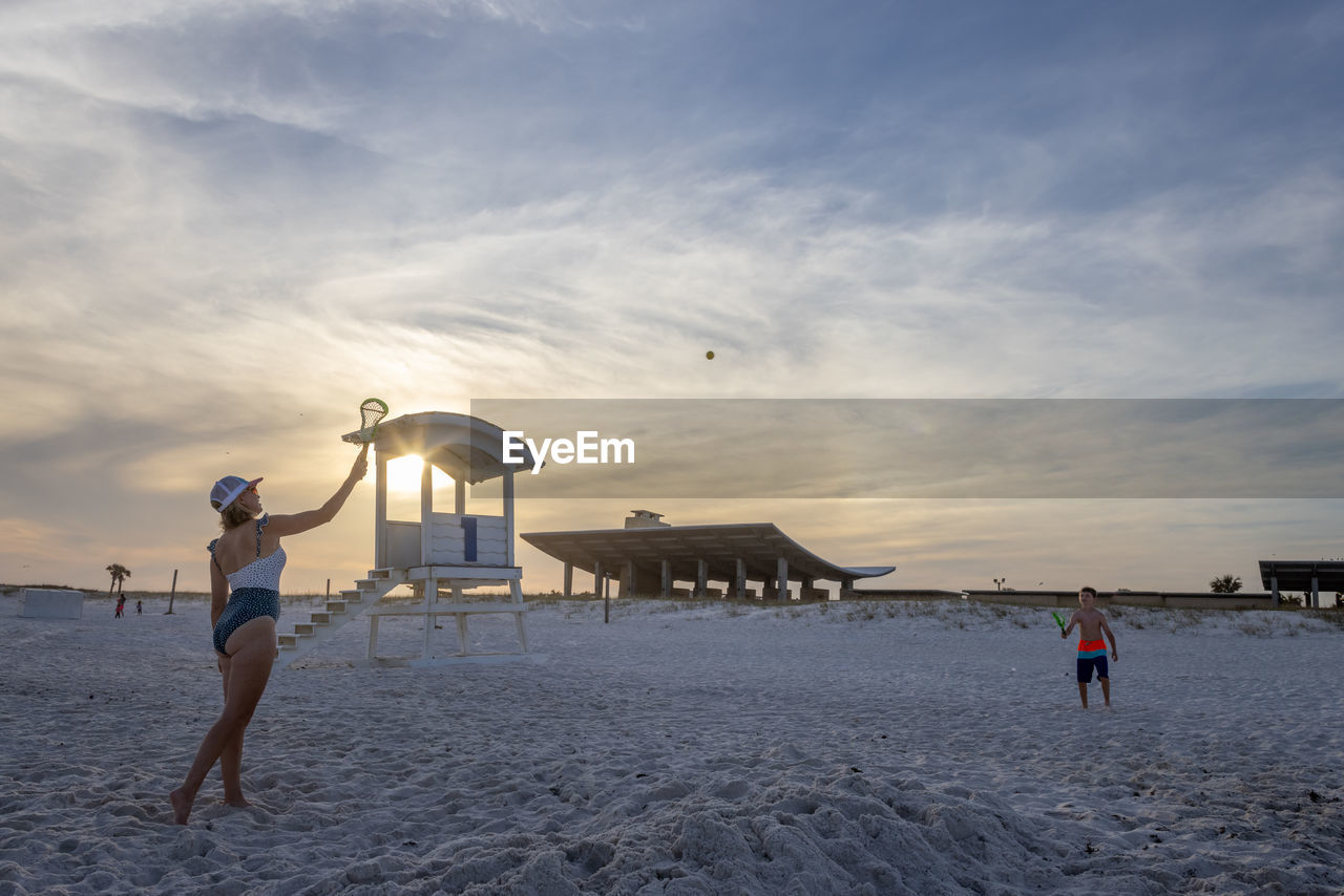 People playing at beach against sky during sunset