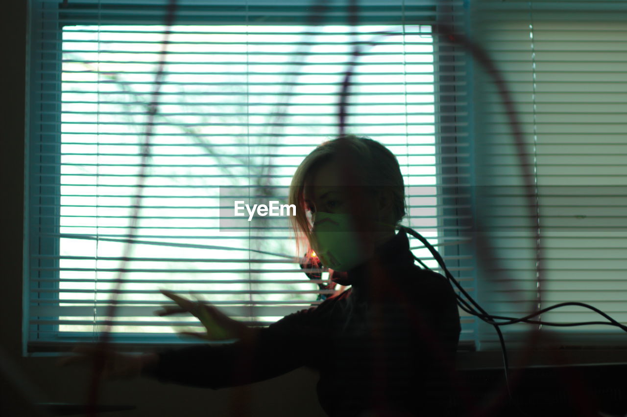 Woman wearing mask while standing by window