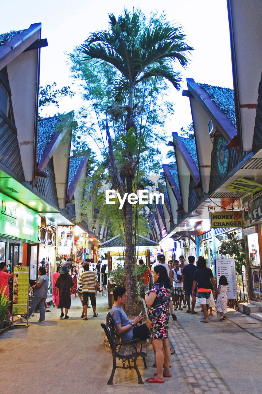 PEOPLE SITTING ON STREET AMIDST BUILDINGS