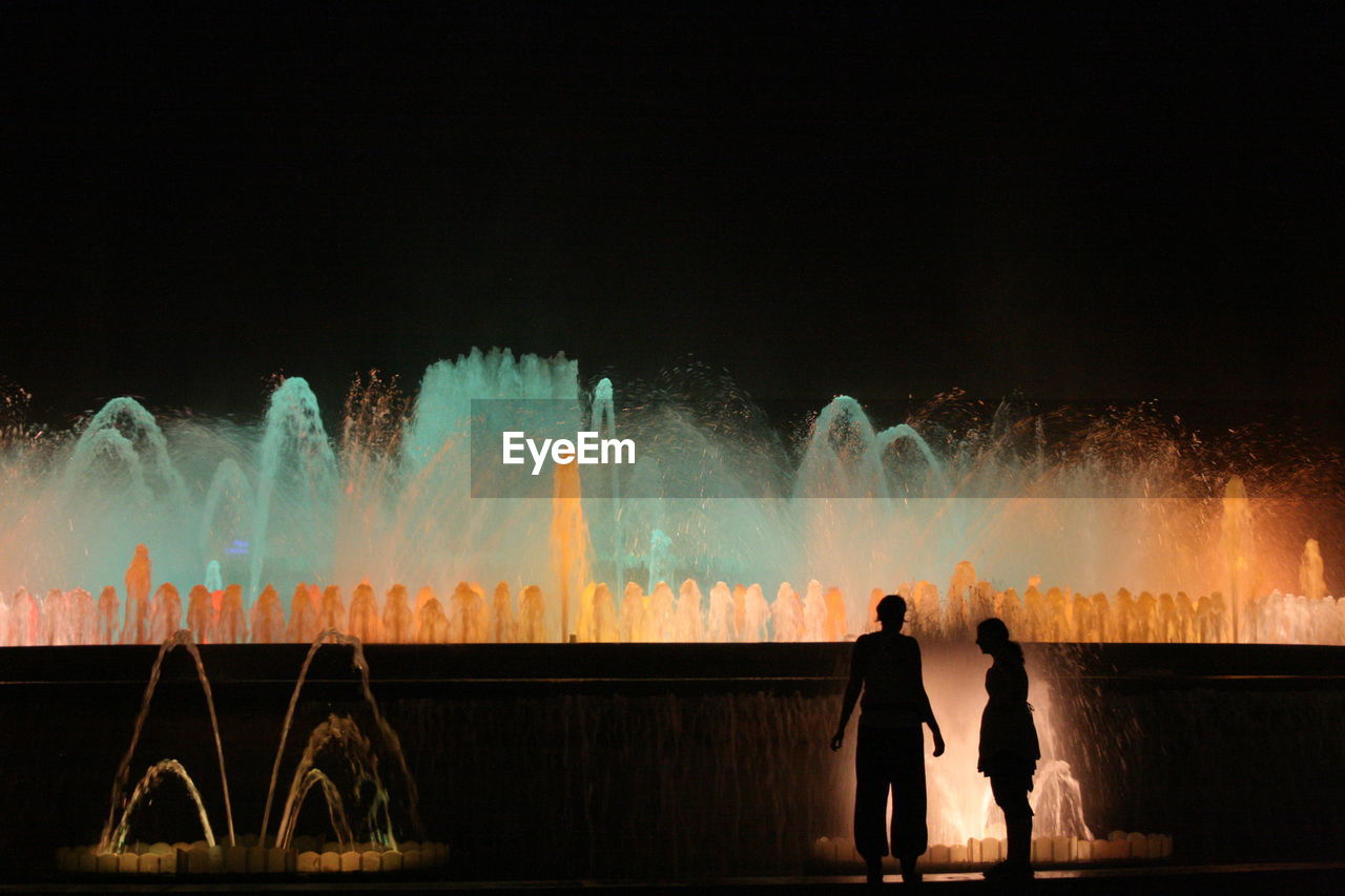 Silhouette women standing by illuminated fountain at plaza de espana