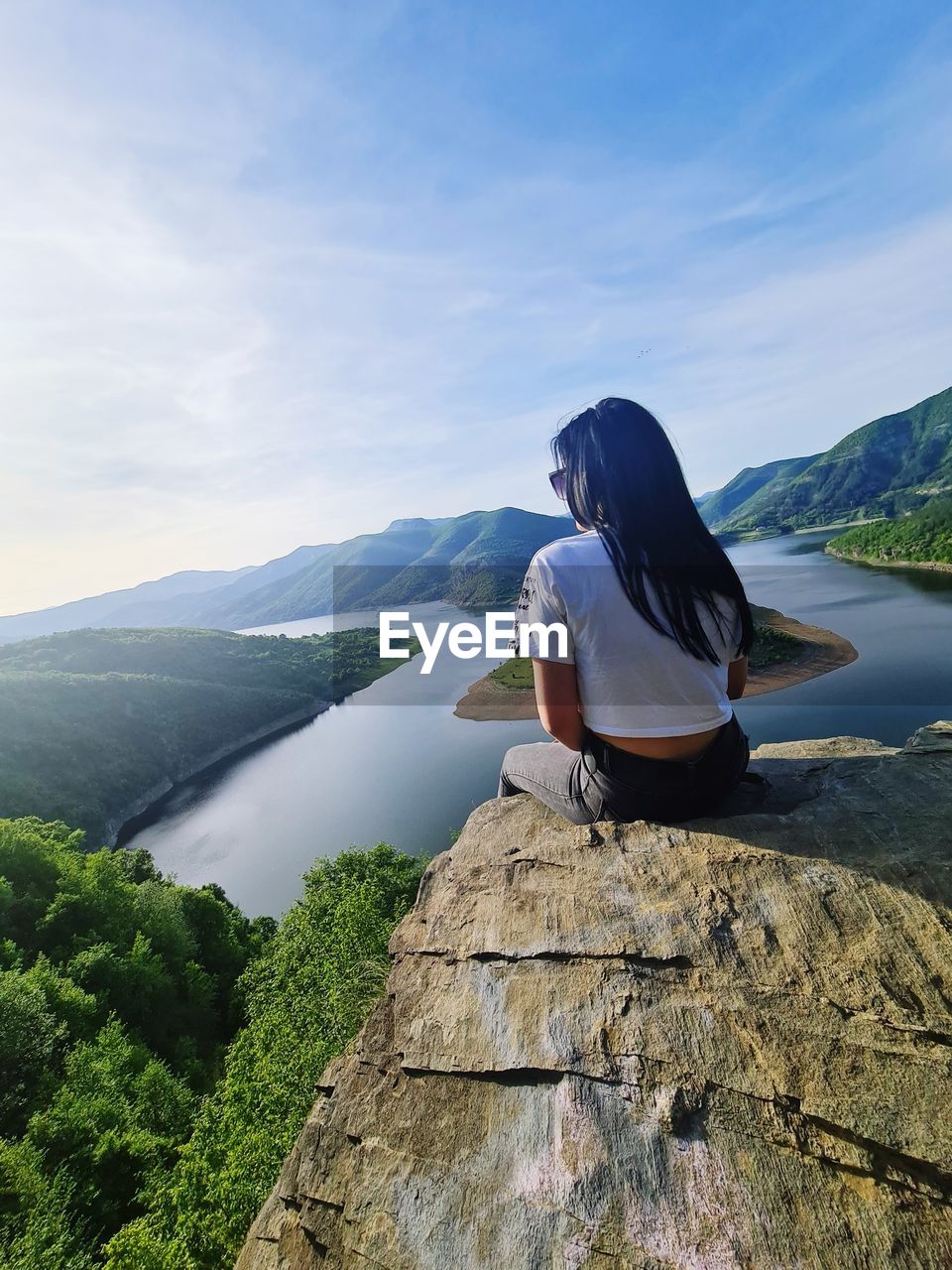 rear view of woman sitting on rock by sea against sky