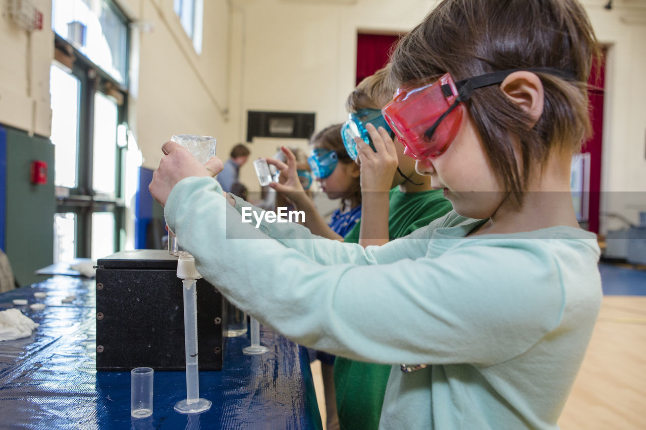 A little girl in safety goggles measures liquid into a test tube