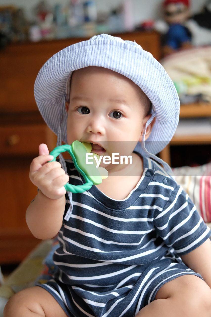 Portrait of cute baby girl with toy in mouth at home