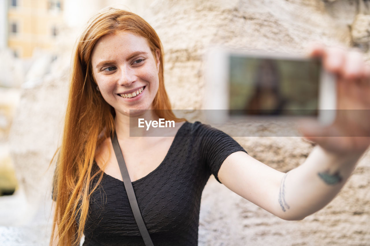 Cheerful redhead woman taking selfie in city