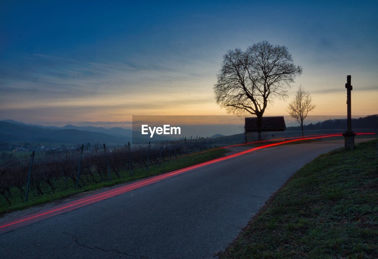 ROAD BY BARE TREES AGAINST SKY AT SUNSET