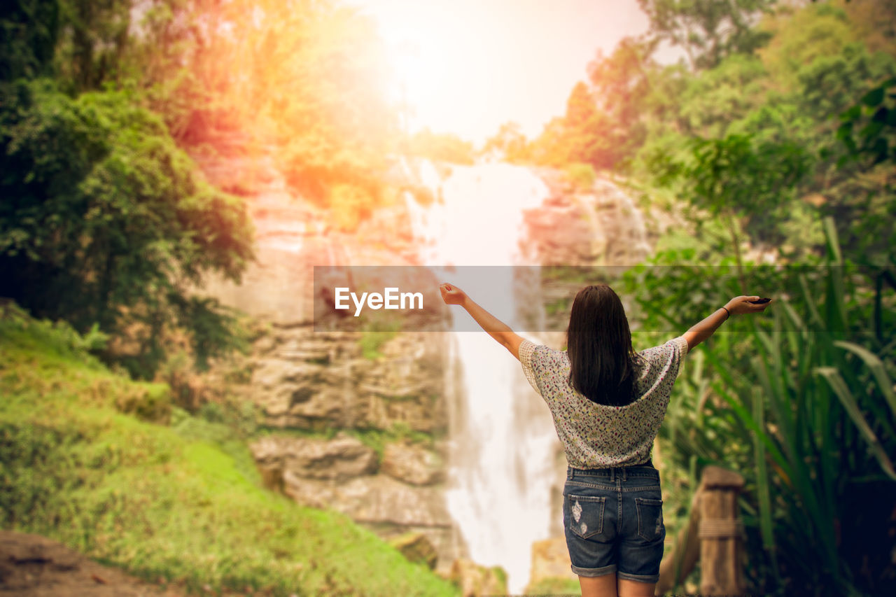 Rear view of teenage girl standing against waterfall