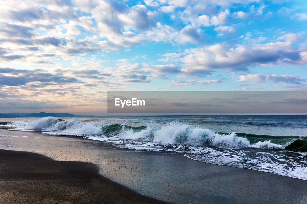 Scenic view of sea with crashing waves against dramatic sky during sunrise