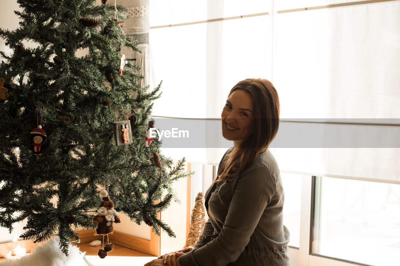 Portrait of smiling woman sitting by christmas tree at home