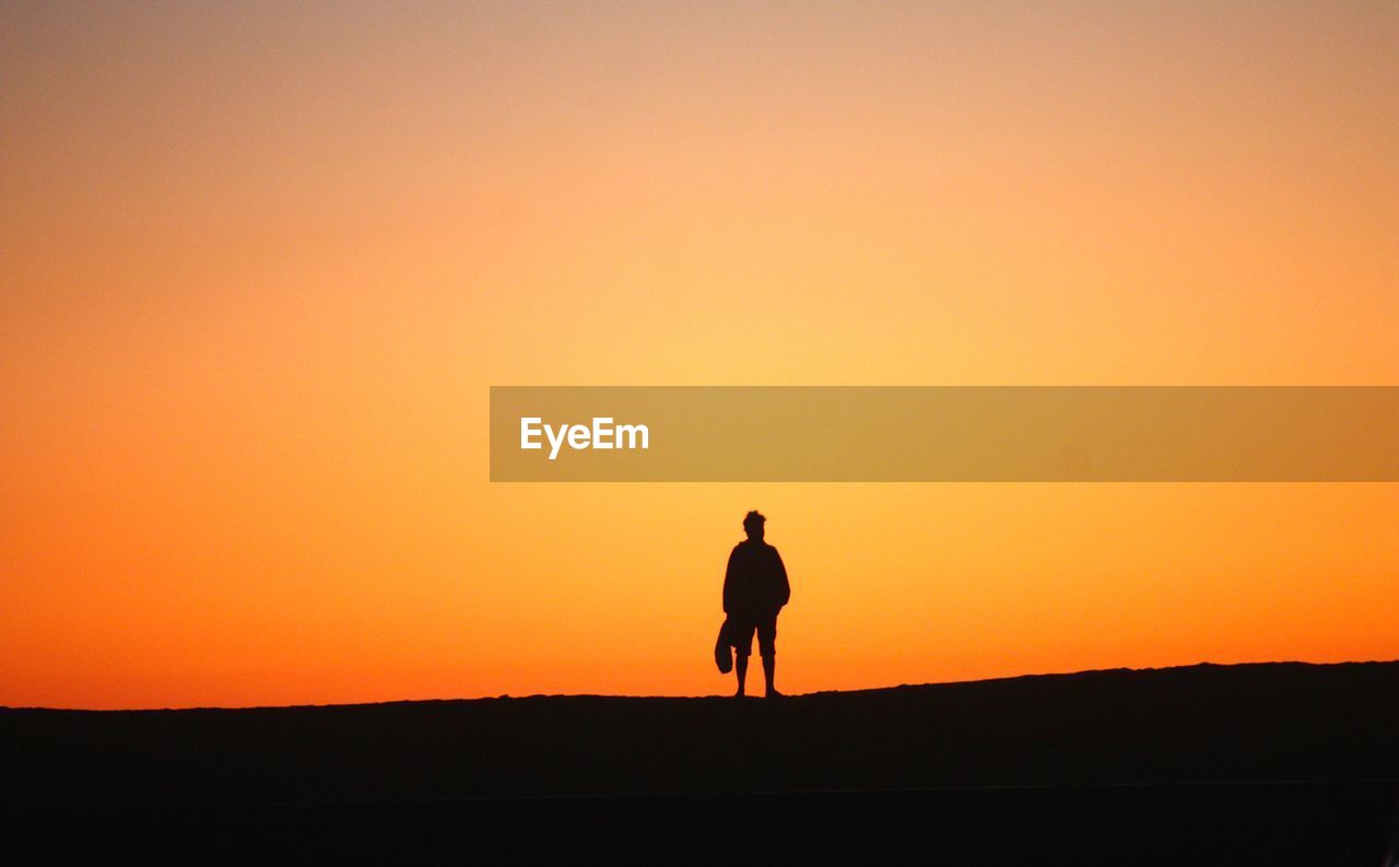 Silhouette man standing on landscape against sky during sunset