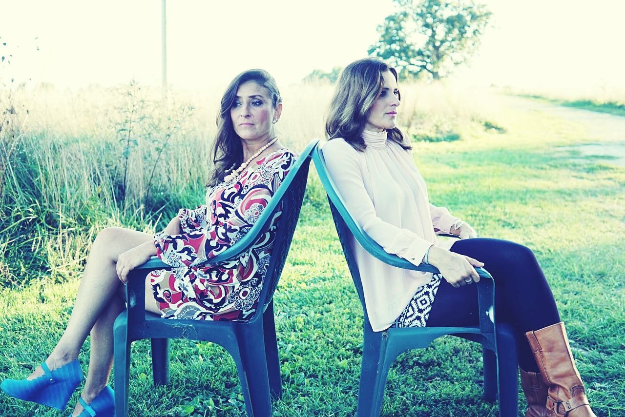 Women sitting back to back on chair over field at yard