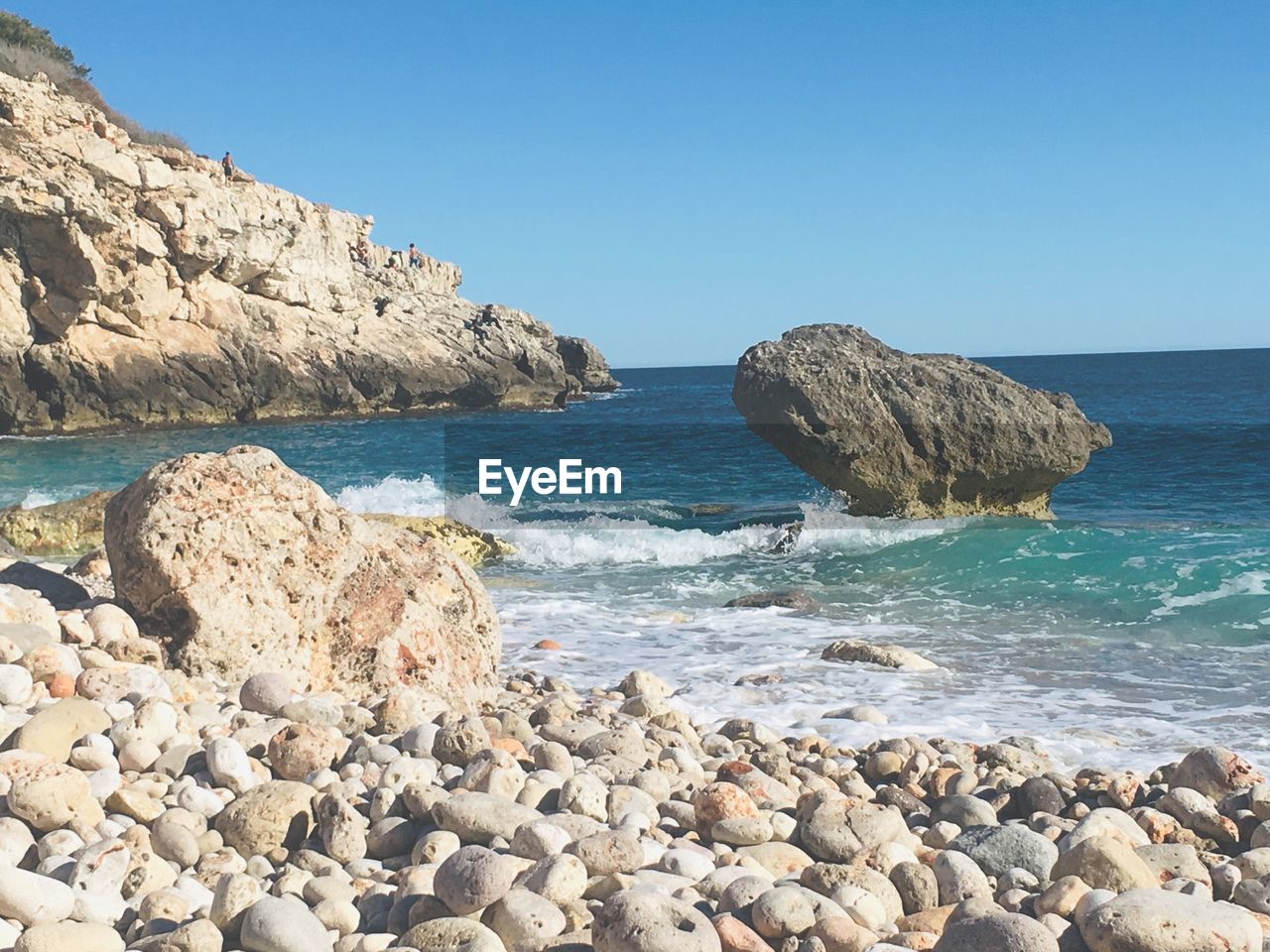 Rocks in sea against clear blue sky