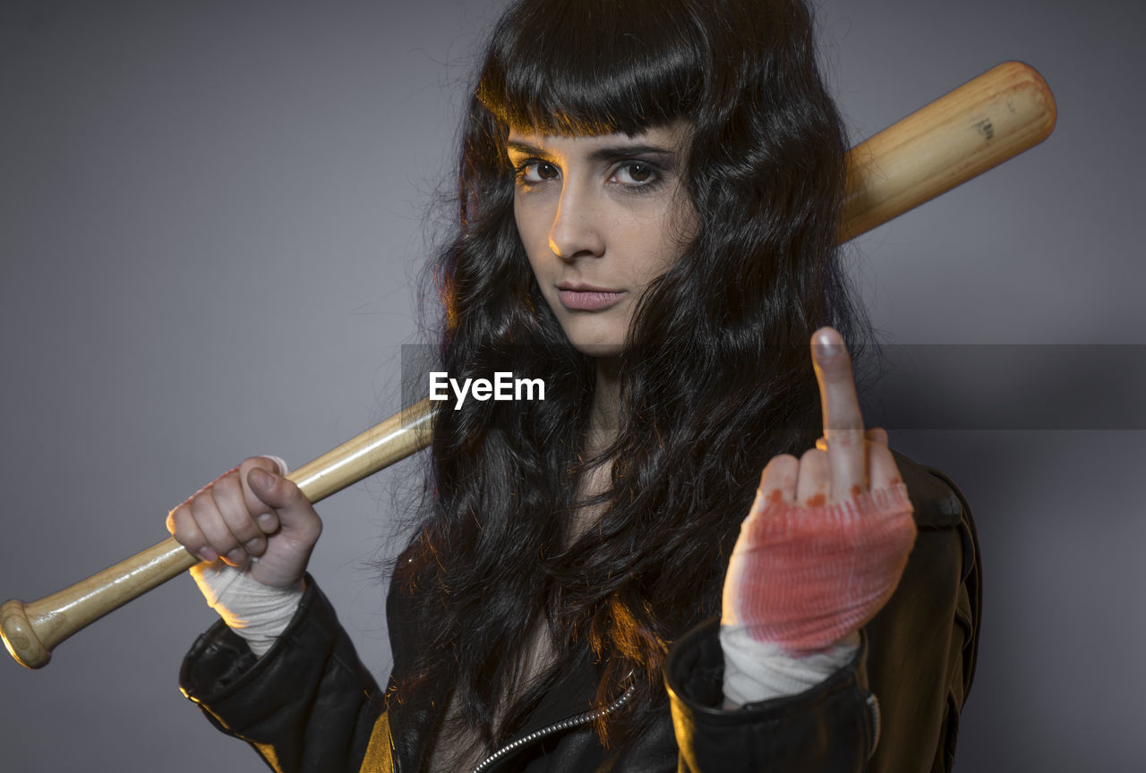 Portrait of young female model holding baseball bat against gray background