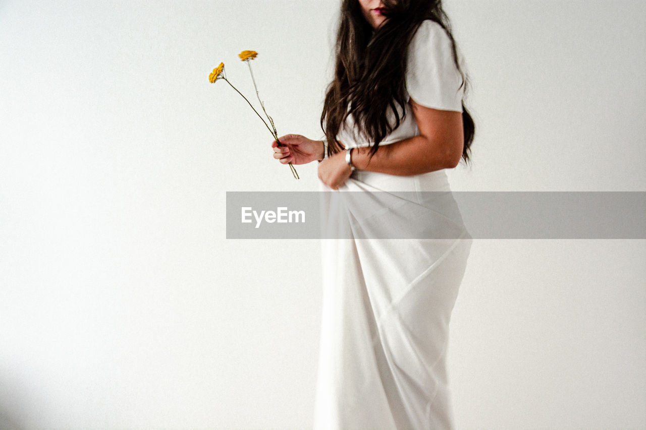 Side view of woman standing against white background holding flowers