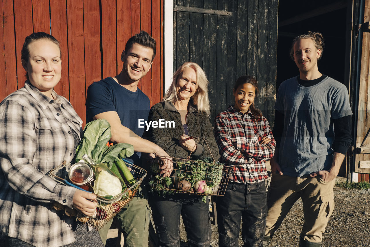 Portrait of male and female farmers with organic vegetables standing outside barn