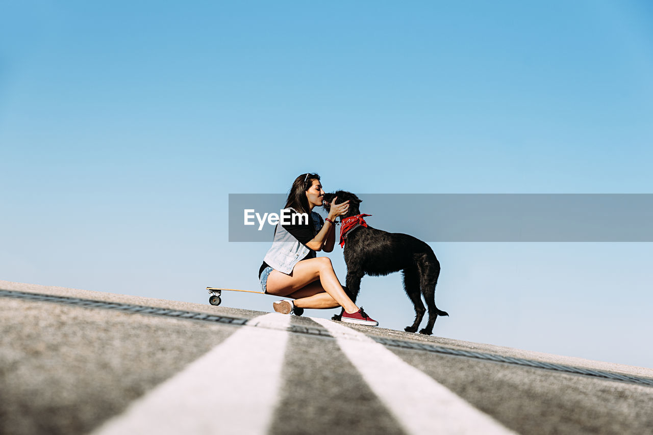 Woman with dog and skateboard against clear blue sky