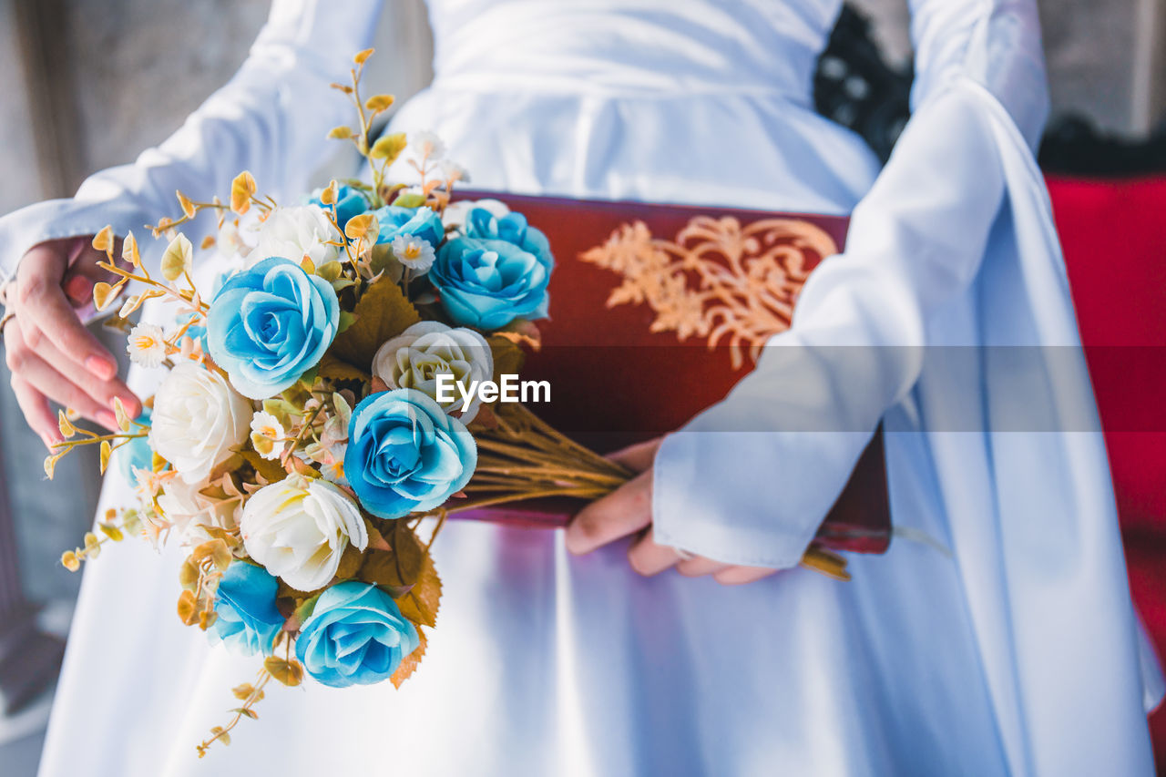 Midsection of woman holding book and flowers