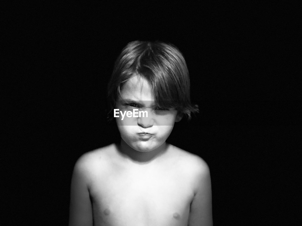 Portrait of shirtless boy sulking against black background