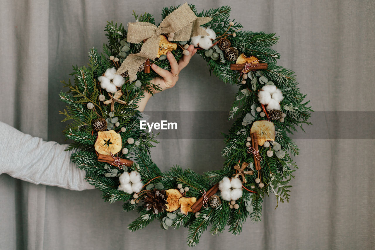 Cropped hand holding wreath against curtain