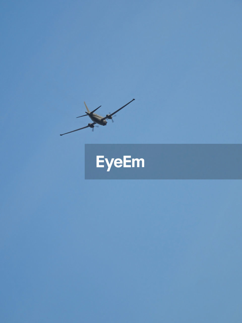 LOW ANGLE VIEW OF AIRPLANE IN FLIGHT AGAINST BLUE SKY