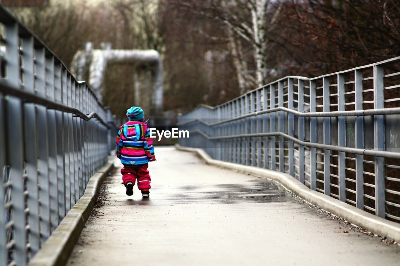 REAR VIEW OF BOY WALKING ON FOOTBRIDGE