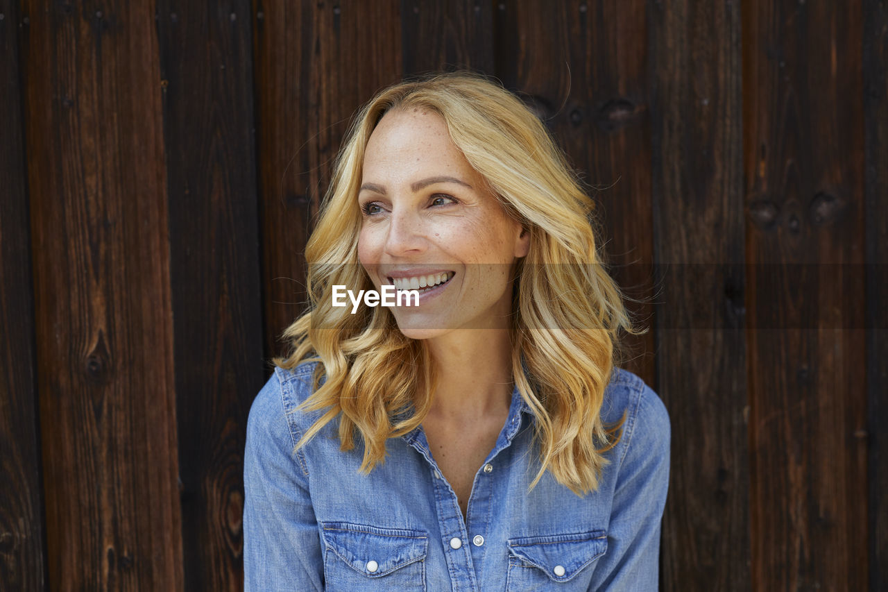 Happy blond woman in front of wooden wall