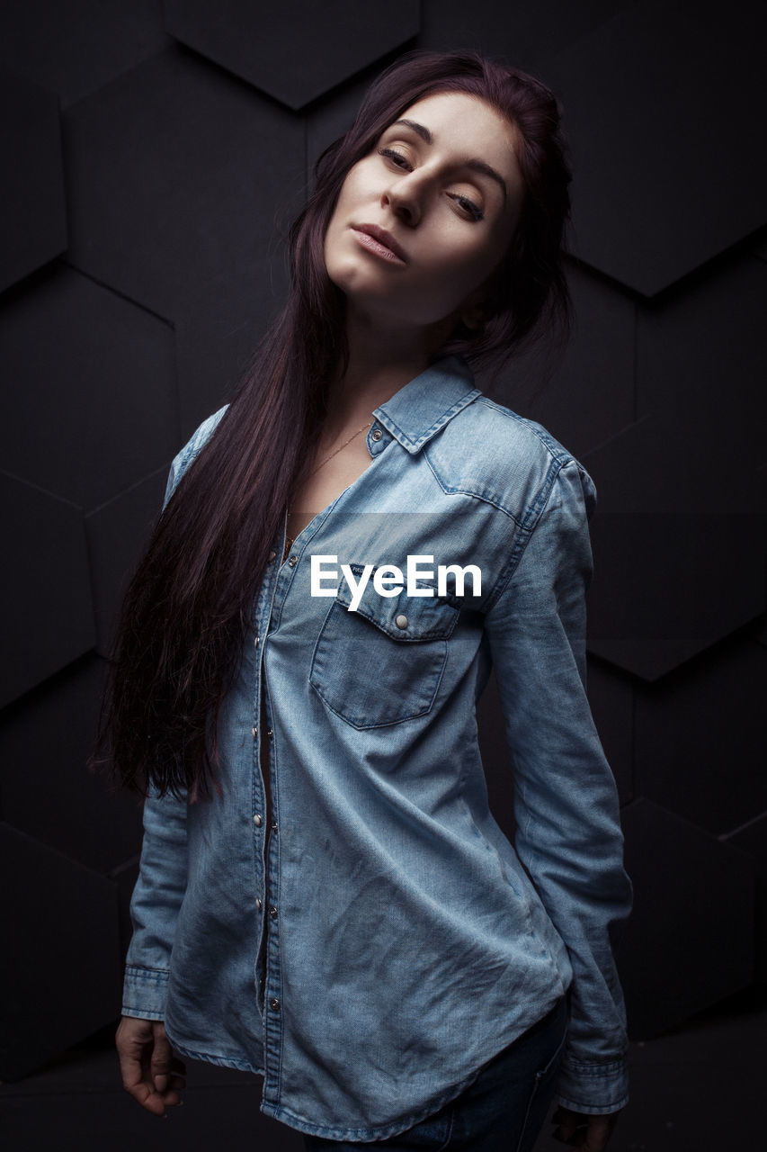 Portrait of young woman standing against wall at home