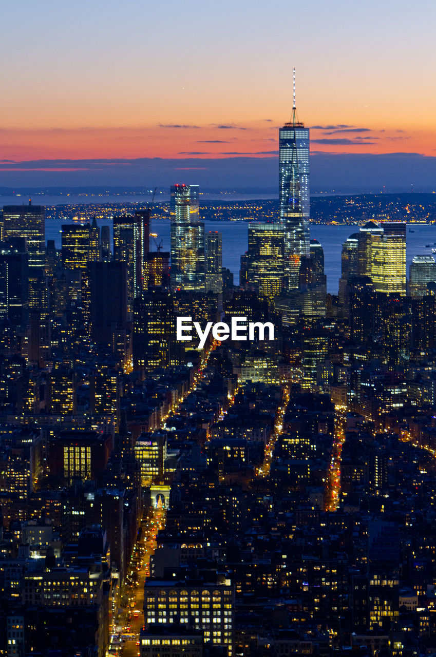 One world trade center in illuminated city against sky during sunset