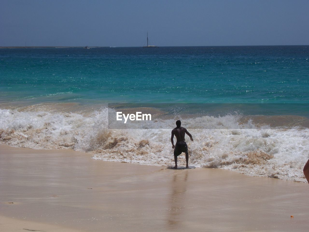 Rear view of shirtless man standing at beach against sky