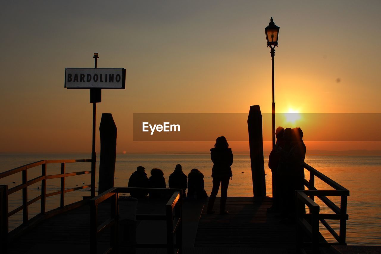 Silhouette people on pier over sea during sunset