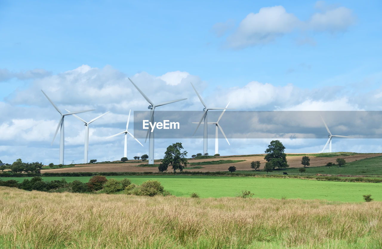 Wind turbines on field against cloudy sky