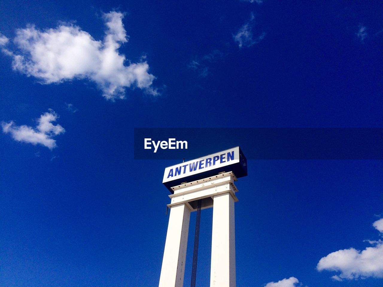 Low angle view of text on gate against blue sky