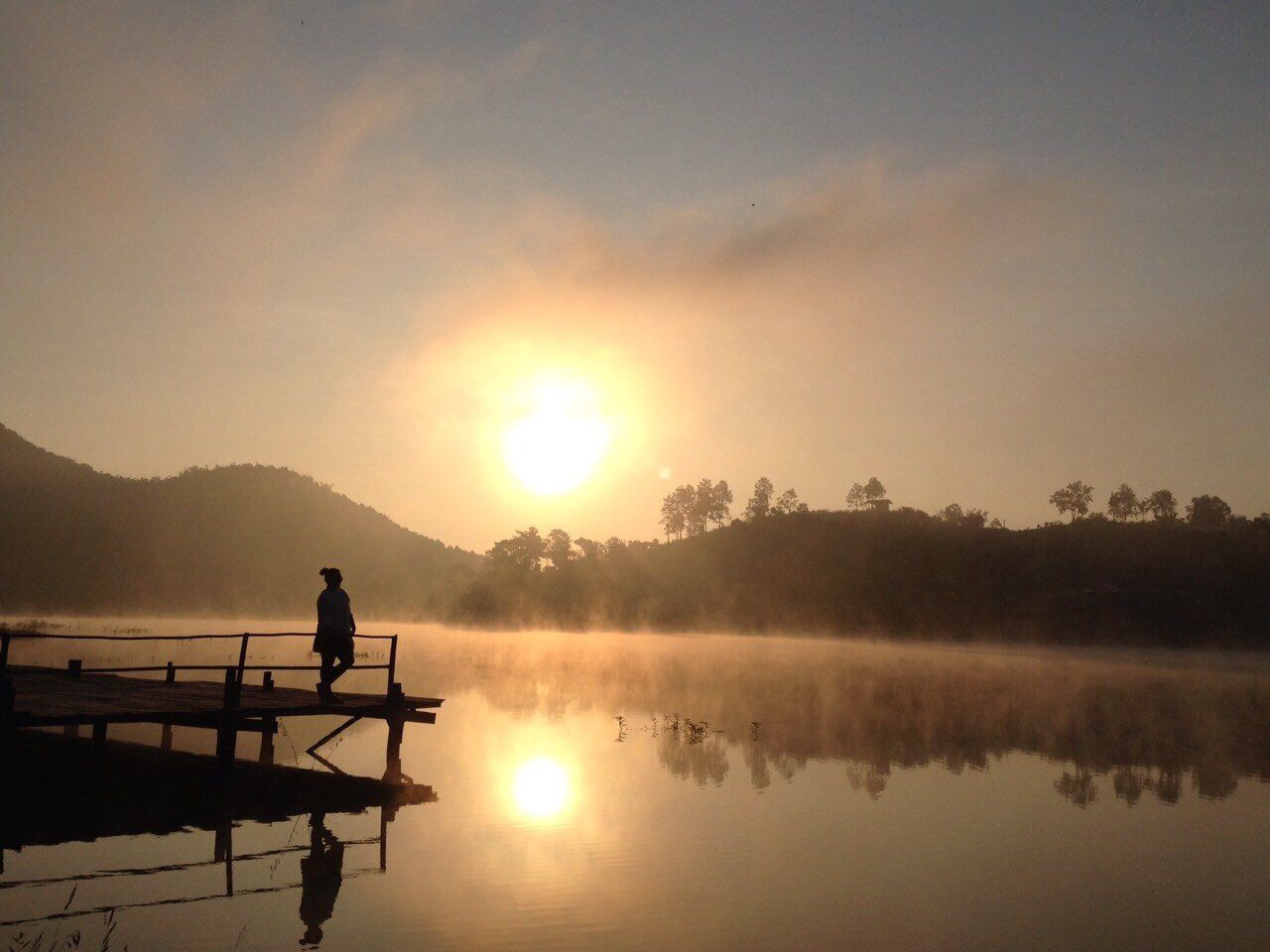 Silhouette of woman standing on pier looking at sunrise