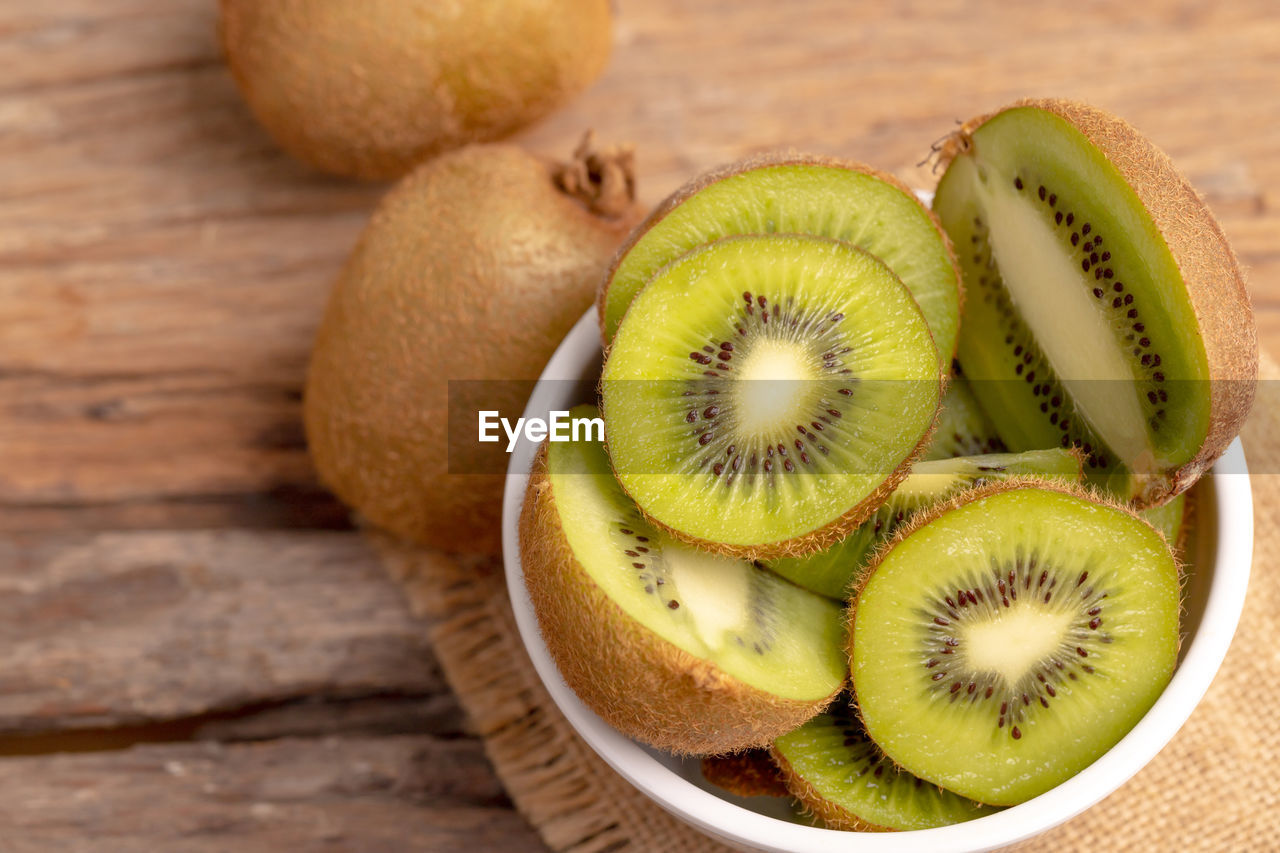 Fresh green kiwis in the white bowl on the brown sack on the old wooden table