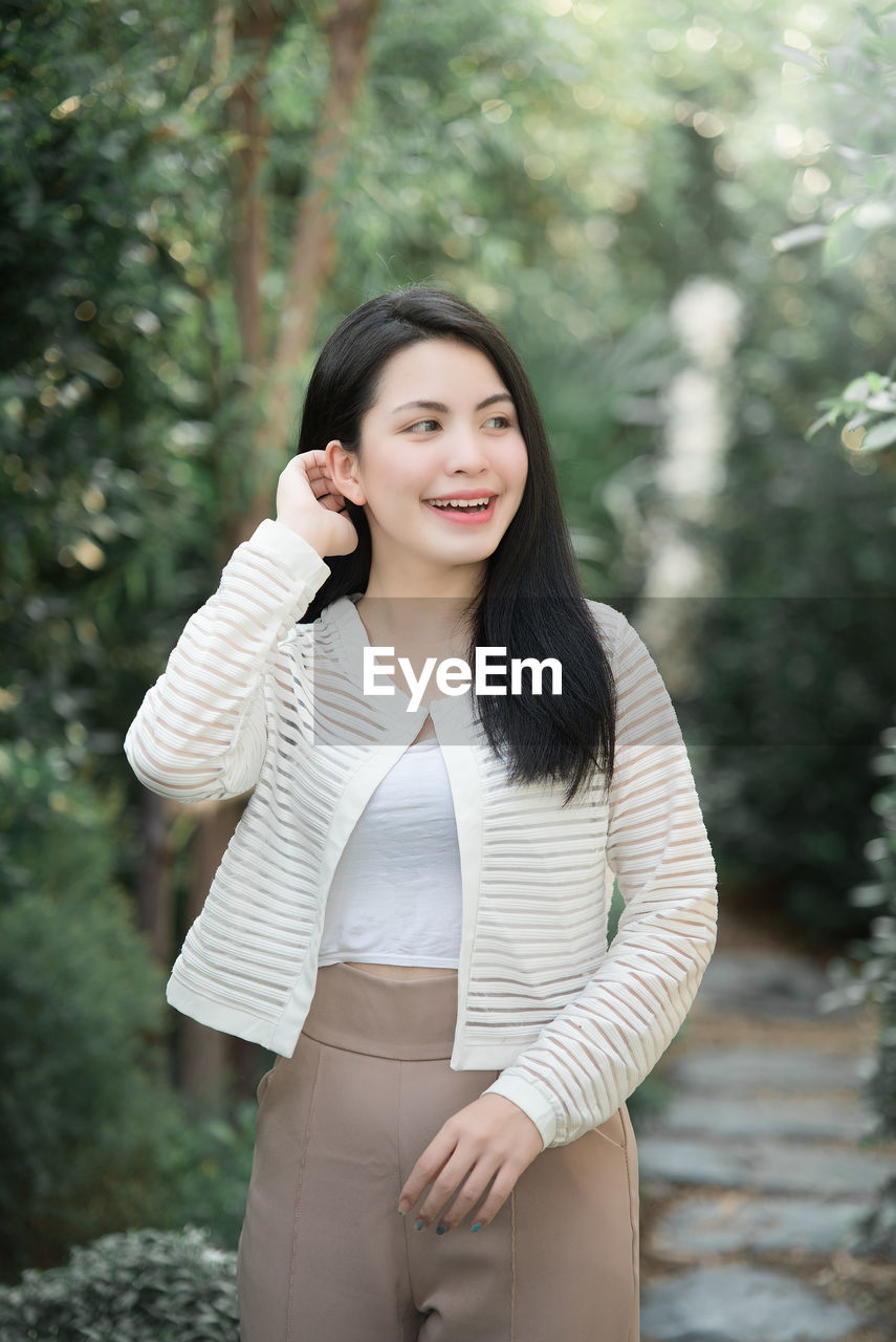 Portrait of young woman standing against tree