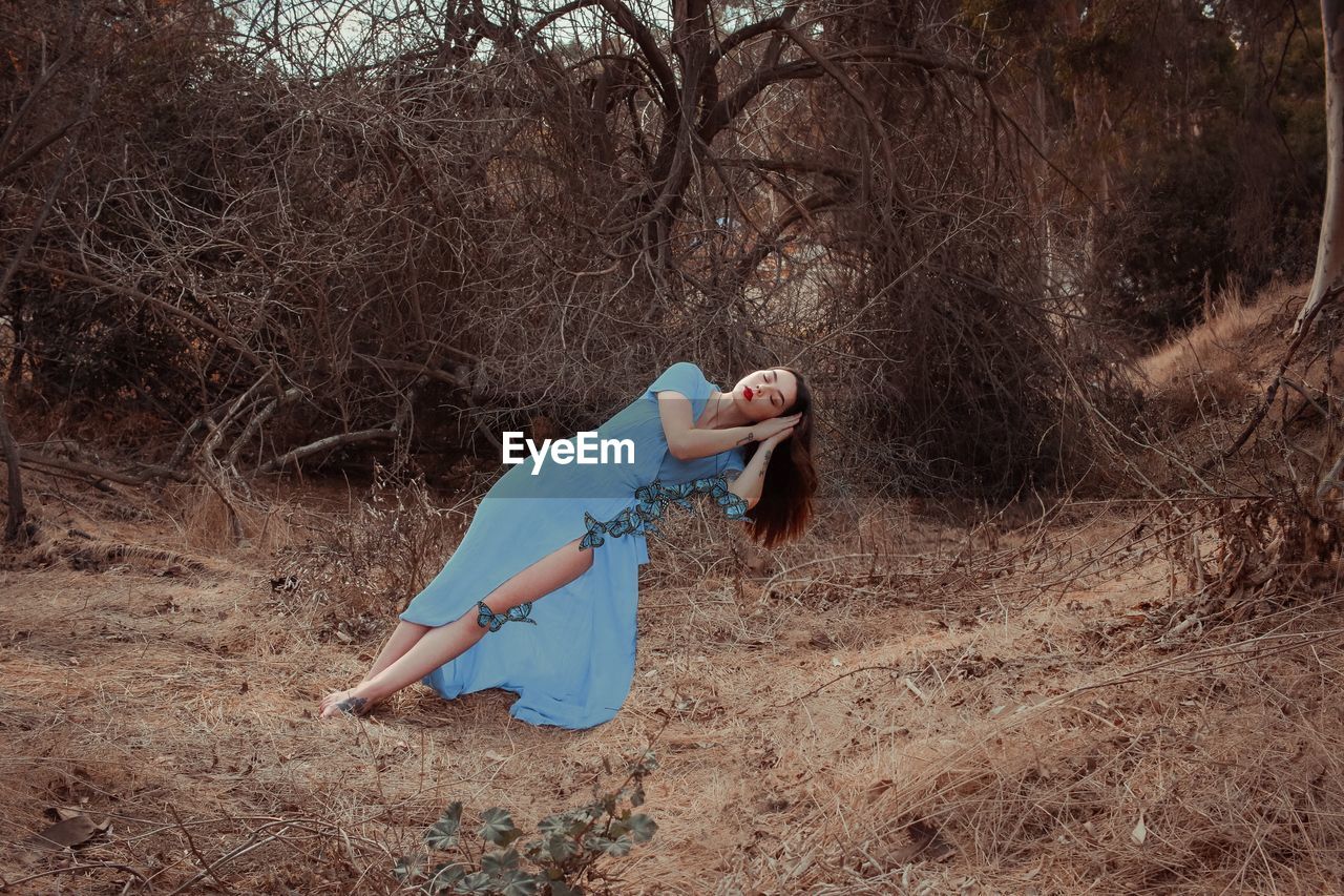 Digital composite image of young woman sleeping on butterflies against bare trees in forest