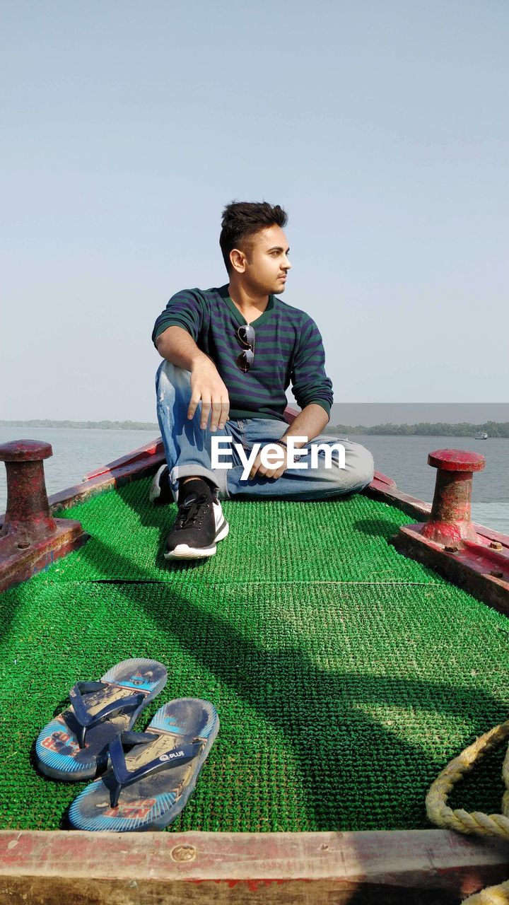 YOUNG MAN SITTING ON BOAT AGAINST SEA