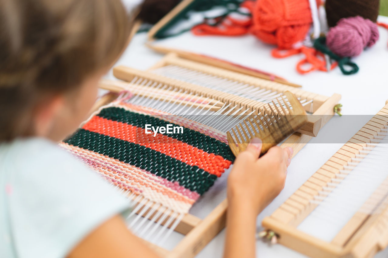 Girl weaving small rug with pattern at masterclass on weaving.