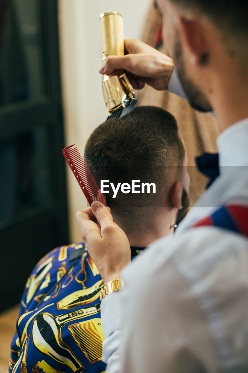 A barber cuts the hair of a customer with a clipper