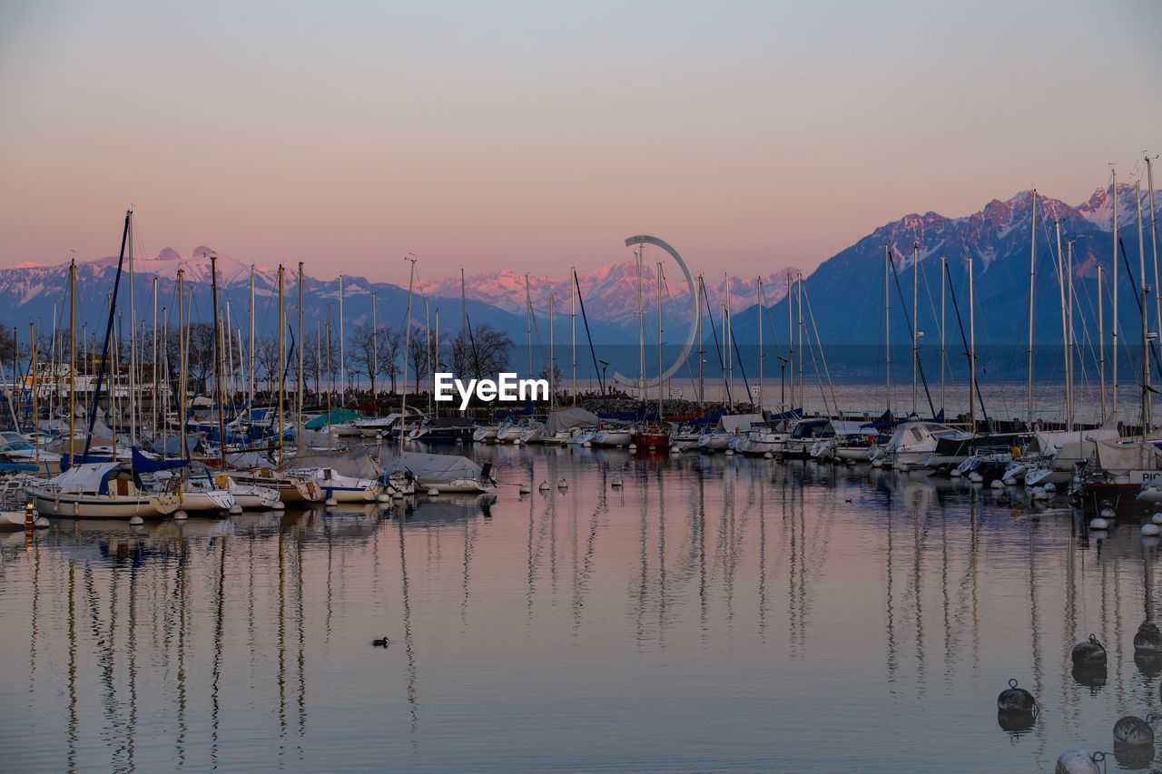 Sailboats moored at harbor against sky during sunset