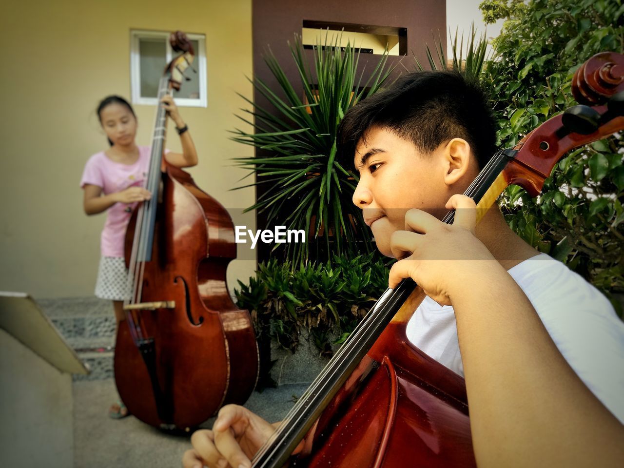 Siblings playing cello outside house