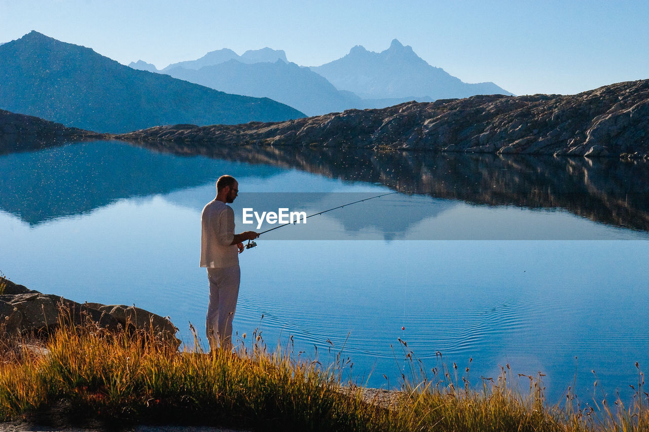 Man fishing at lake against sky