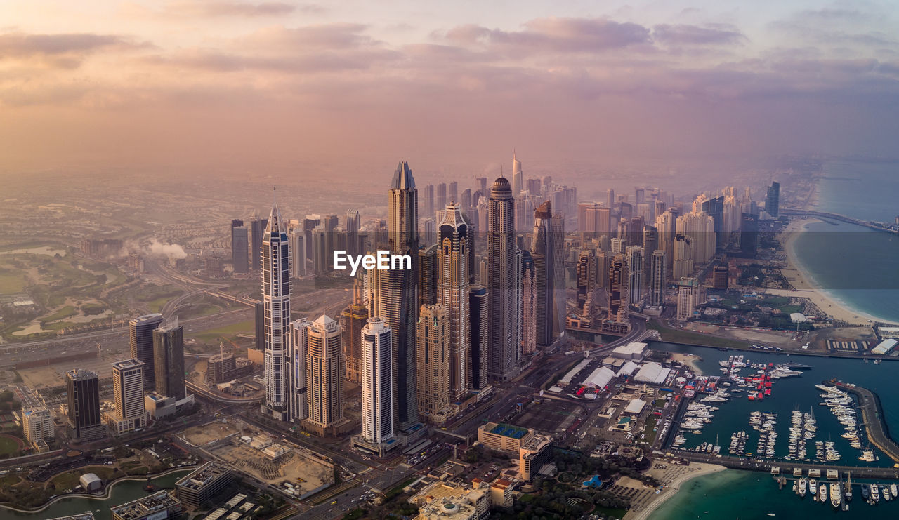 HIGH ANGLE VIEW OF MODERN BUILDINGS IN CITY AGAINST SKY DURING SUNSET