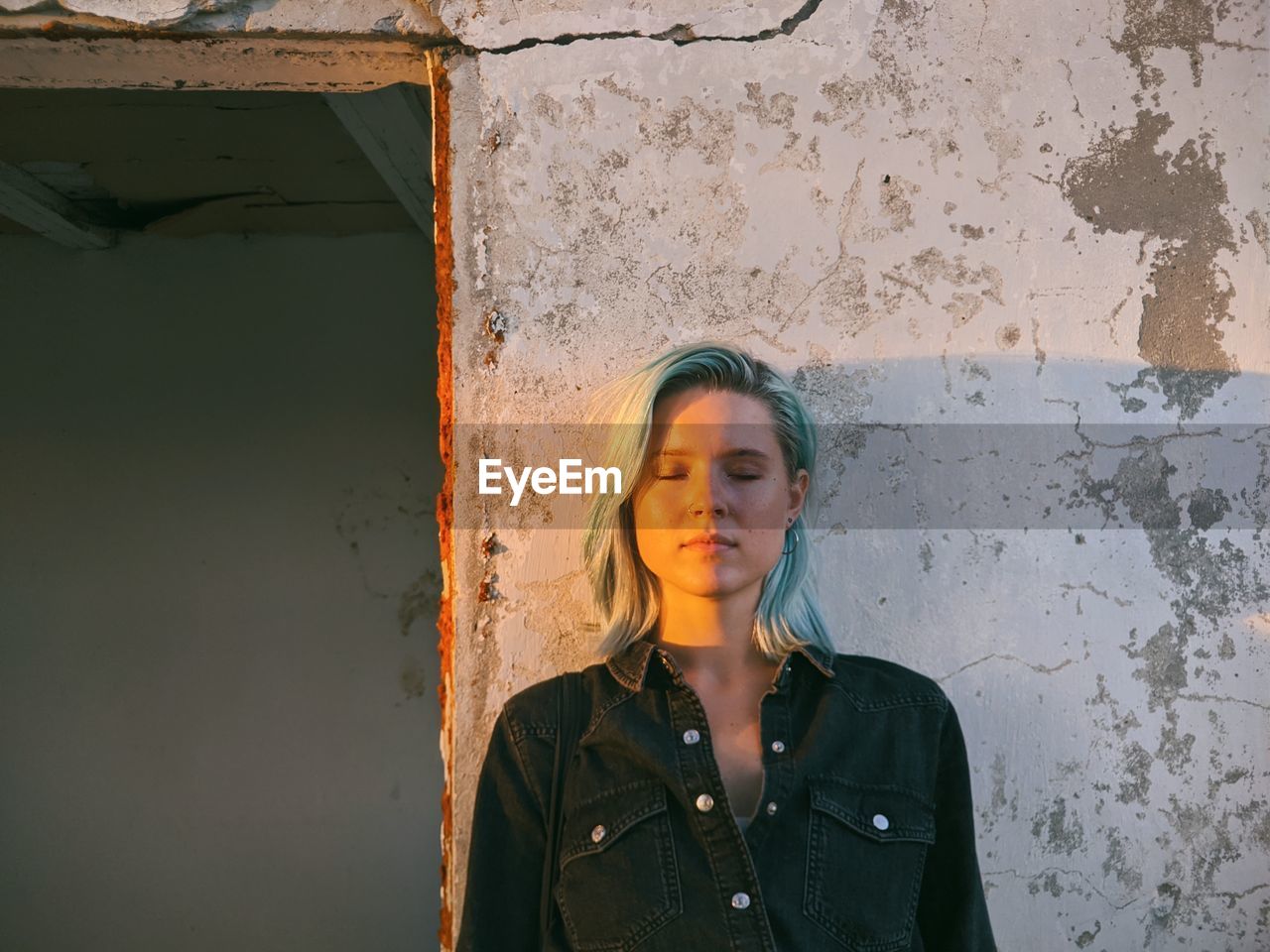 Young woman with closed eyes standing against wall