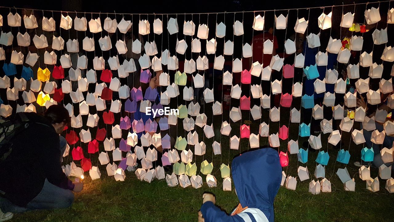 Rear view of man igniting candle by lanterns hanging from string at night